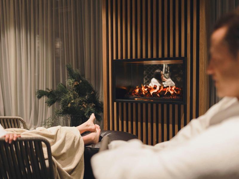 Zwei Menschen entspannen sich vor einem modernen Kamin, warme Beleuchtung, gemütliche Atmosphäre.