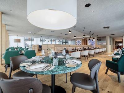 Ristorante moderno con tavoli rotondi, sedie verdi e grigie e soffitto in legno chiaro.