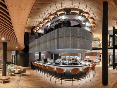 Nowoczesny bar hotelowy z zakrzywionym barem, skórzanymi stołkami i ciepłym drewnianym wystrojem.