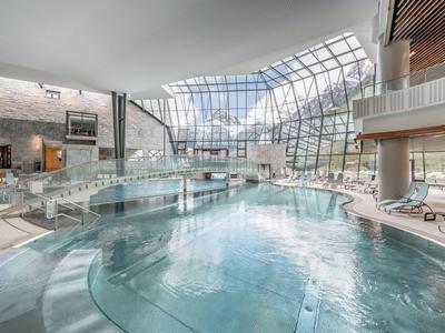 Grande piscina interna con tetto in vetro e lettini in una spa di un hotel moderno.