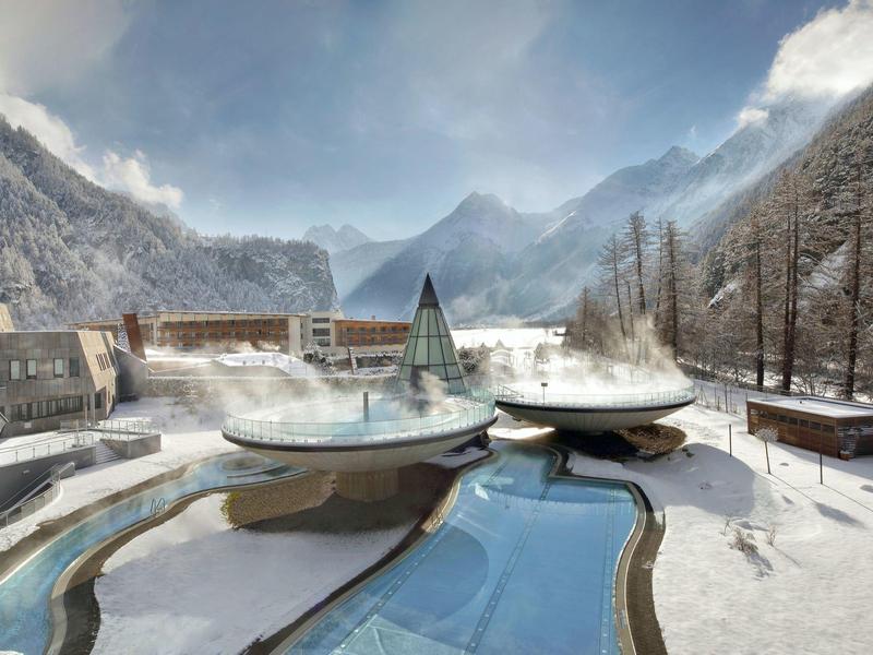 Terme invernali con piscine curve in una valle montuosa innevata.