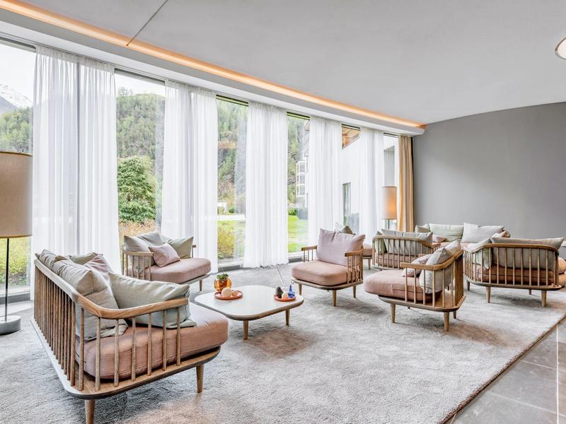 Lounge luminosa con grandi finestre, eleganti poltrone e tavoli in tonalità neutre.