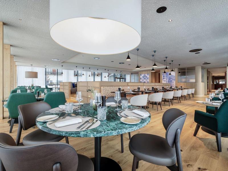 Ristorante moderno con tavoli rotondi, sedie verdi e grigie e soffitto in legno chiaro.