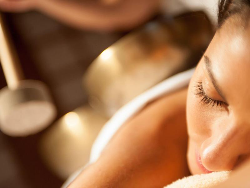 Donna che si rilassa durante un trattamento spa con ciotole sonore sullo sfondo.