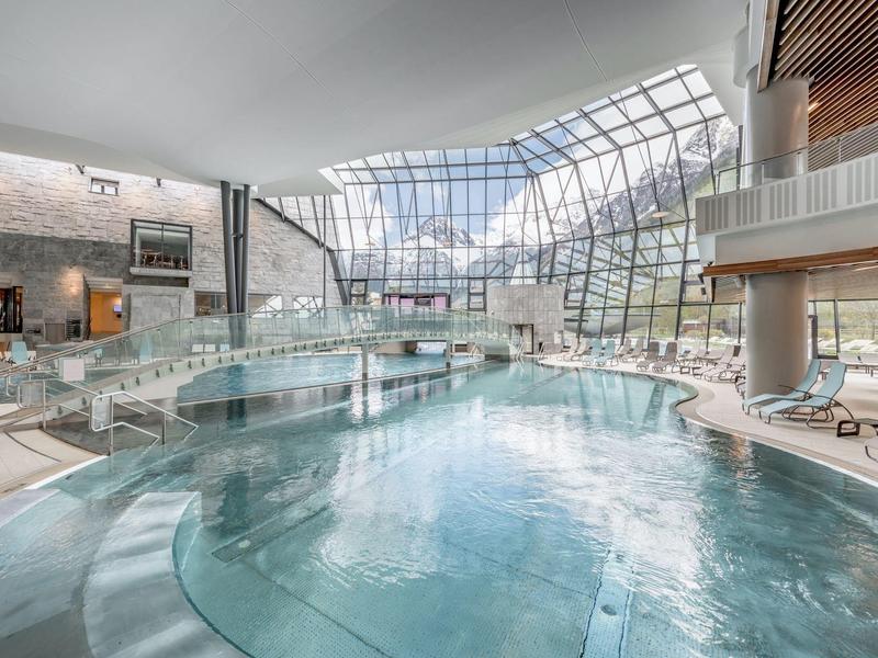 Grande piscina interna con tetto in vetro e lettini in una spa di un hotel moderno.