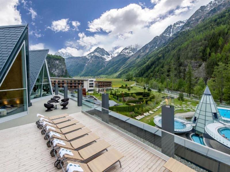 Vista di un hotel con lettini, giardino e montagne sullo sfondo in una giornata di sole.