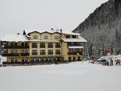 Ein gelbes Hotelgebäude mit geschwungenen Balkonen umgeben von Schnee und Winterwald.