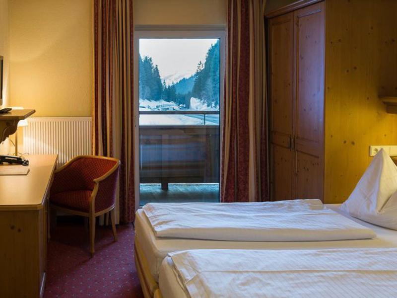 Chambre d'hôtel confortable avec deux lits, bureau, TV et balcon avec vue sur la montagne.