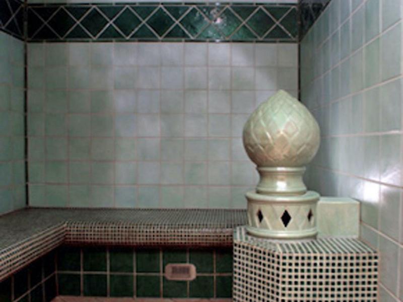 Salle de hammam traditionnelle avec des bancs carrelés et un poêle décoratif au centre.