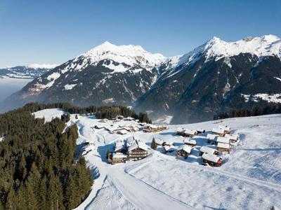 Schneebedeckte Berglandschaft mit Dorf, Nadelwald und strahlend blauem Himmel im Hintergrund.