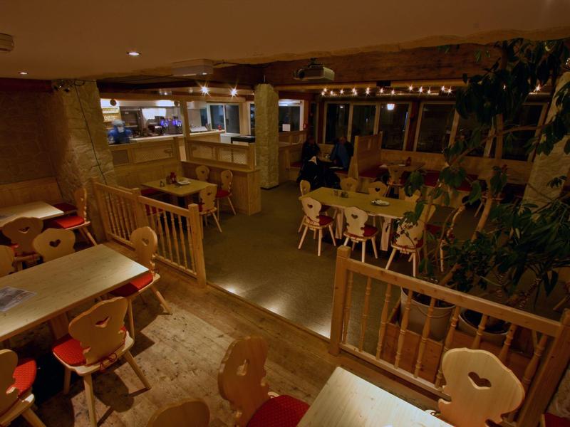 Gemütliches Café mit Holzstühlen und Tischen, warmes Licht und Pflanzen in der Ecke.