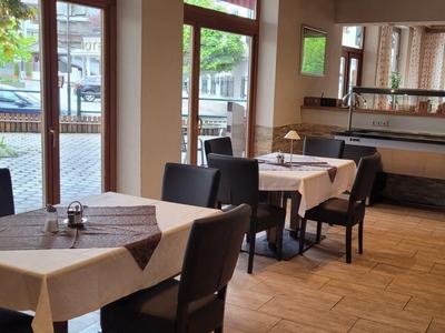 Jasna jadalnia z kwadratowymi stołami i dużymi oknami z widokiem na zewnątrz.