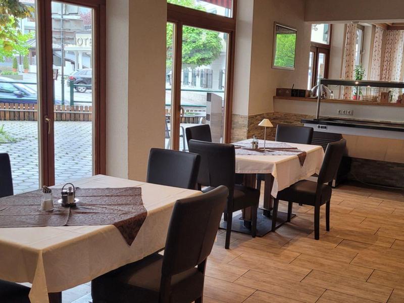 Gastraum mit braunen Stühlen, weißen Tischen, großen Fenstern und Holzboden in hellem Ambiente.