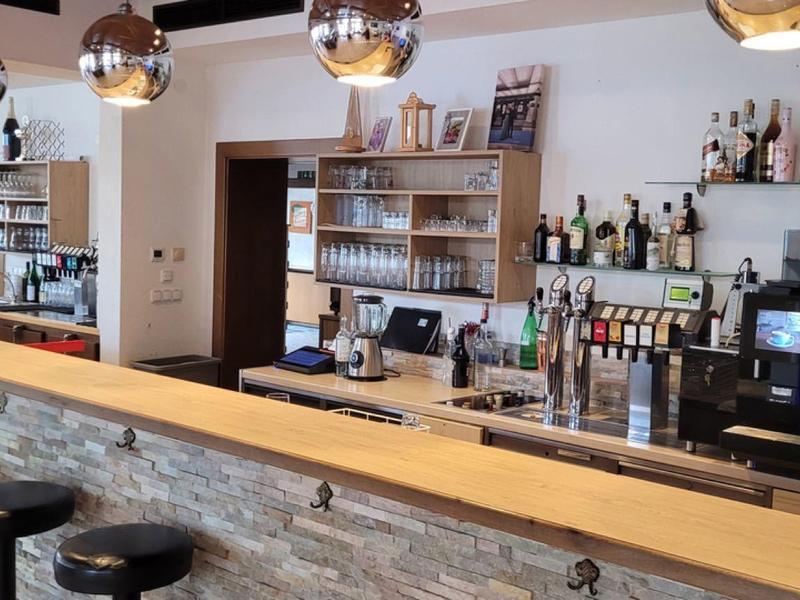 Moderne Bar mit langer Holztheke, schwarzen Hockern und Regalen voller Flaschen und Gläser.