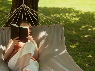 Personne allongée dans un hamac sous un arbre en train de lire un livre au soleil.