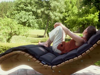 Personne se détendant sur une chaise longue noire dans un jardin par une journée ensoleillée.