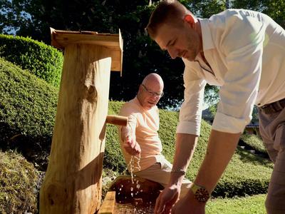 Deux hommes puisent de l'eau dans une fontaine extérieure en bois rustique.