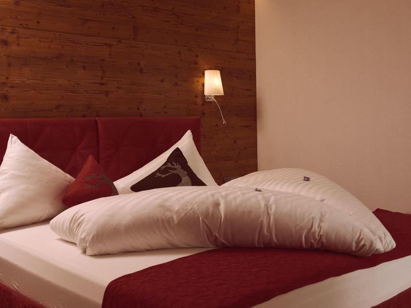 Gemütliches Schlafzimmer mit rotem Bett, weißen Kissen und Holzpaneel an der Wand.