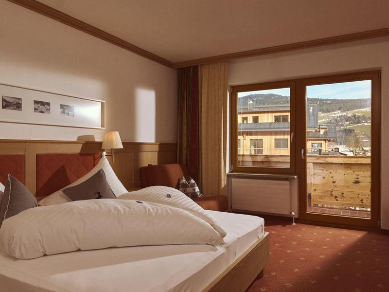 Gemütliches Hotelzimmer mit großem Bett, warmen Holzakzenten und Balkon mit Bergblick.