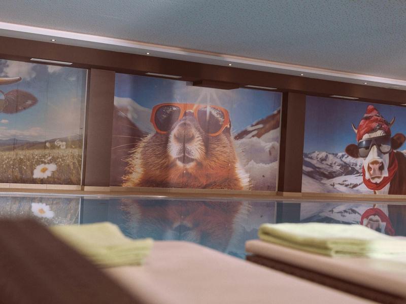 Blick auf ein Hallenbad mit farbenfrohen Tiermotiven an der Wand und Liegetüchern im Vordergrund.