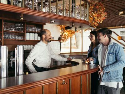 Two guests talk to bartender at wooden bar in a cozy hotel lounge.
