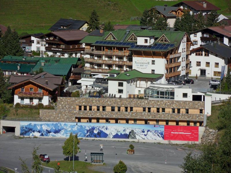 Multi-story hotel surrounded by traditional alpine houses in a green valley.