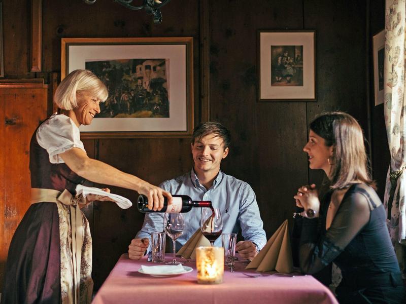 A waitress pours wine for a couple in a cozy restaurant.