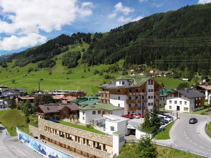 Mountain village with houses and green hills under a blue sky.