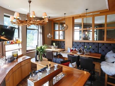 Area accogliente di hotel o ristorante con mobili in legno, angoli salotto e lampadario decorativo.