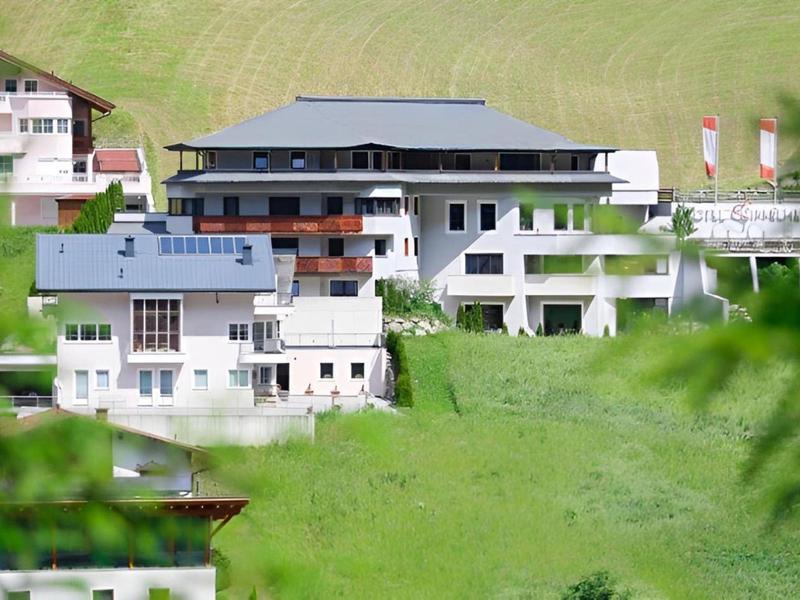 Mehrere weiße Häuser mit dunklen Dächern stehen auf einem grünen Hügel in ländlicher Umgebung.