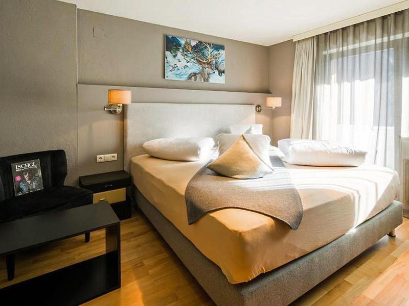 Ein helles Schlafzimmer mit zwei Einzelbetten, hellgrauem Kopfteil, Holzfußboden und großem Fenster.