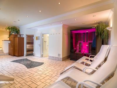 Moderner Wellnessraum mit weißen Liegen, hellen Kacheln und pink beleuchtetem Sauna-Bereich.