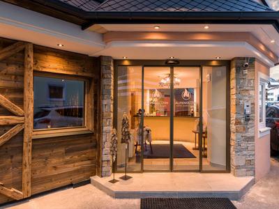 Wejście do hotelu z dużymi szklanymi i drewnianymi drzwiami, ciepłe oświetlenie.