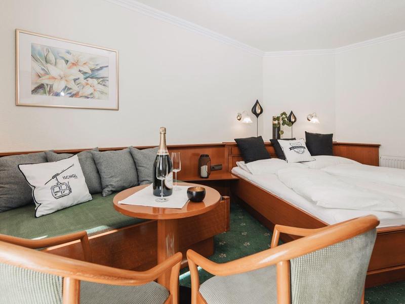 Gemütliches Zimmer mit Doppelbett, Sofa, kleinem Holztisch und zwei Stühlen in warmen Farben.