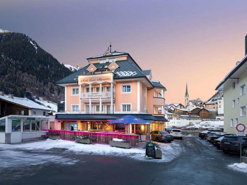 Ein mehrstöckiges Gebäude in Alpenort bei Dämmerung, umgeben von schneebedeckten Bergen.