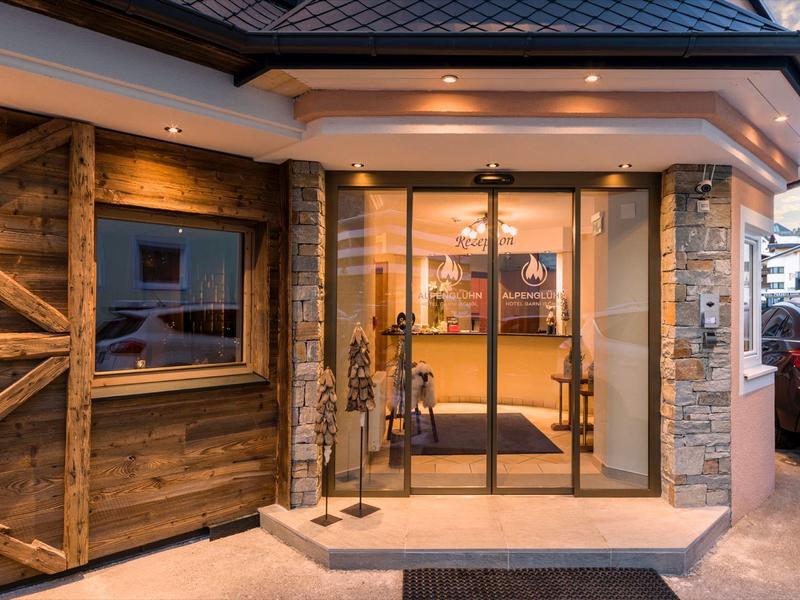 Eingang eines Gebäudes mit großer Glastür, Holzverkleidung und warmem Innenlicht.