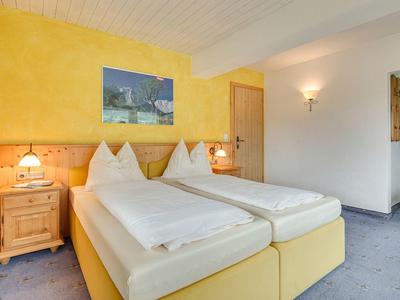 Camera doppia luminosa con parete gialla, due letti singoli e illuminazione accogliente.