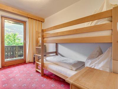 Piccola camera d'hotel con letto a castello, tappeto rosso e balcone con vista sul verde.