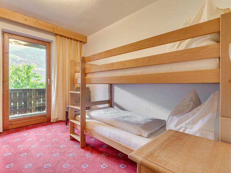 Piccola camera d'hotel con letto a castello, tappeto rosso e balcone con vista sul verde.