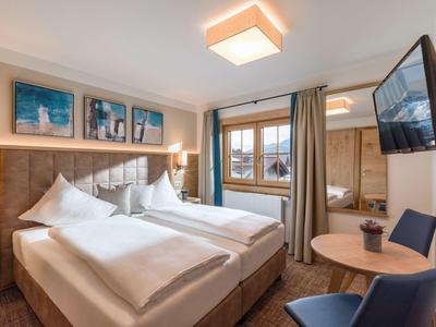 Gemütliches Hotelzimmer mit zwei Einzelbetten, Holzdekor, großem Fenster und modernem TV.