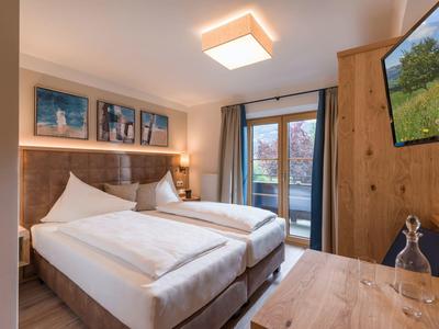 Gemütliches Doppelzimmer mit zwei Betten, Holzvertäfelung und Zugang zu Balkon oder Terrasse.