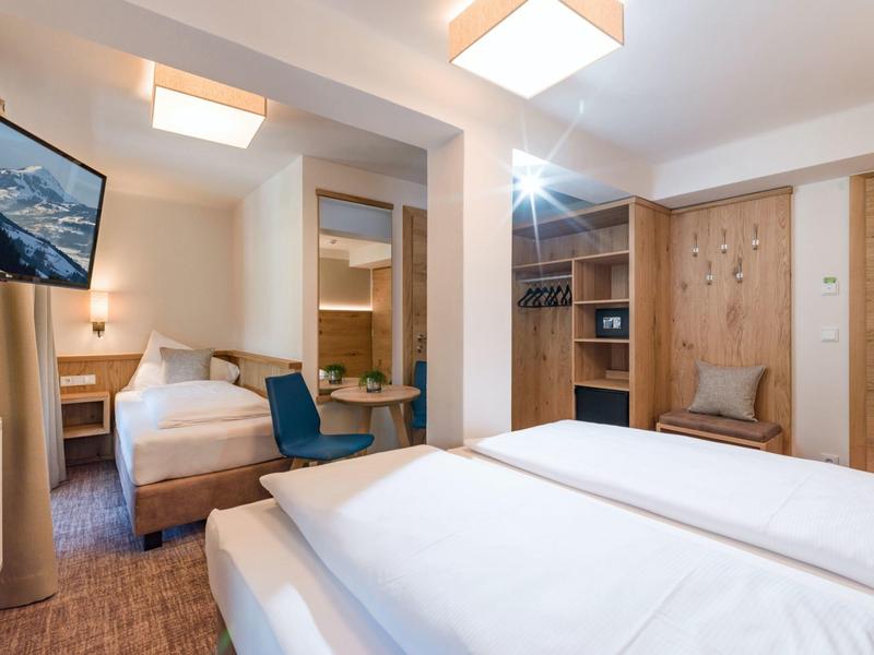 Modernes Hotelzimmer mit zwei Betten, Holzmöbeln, Fernseher und gemütlichem Sitzbereich.