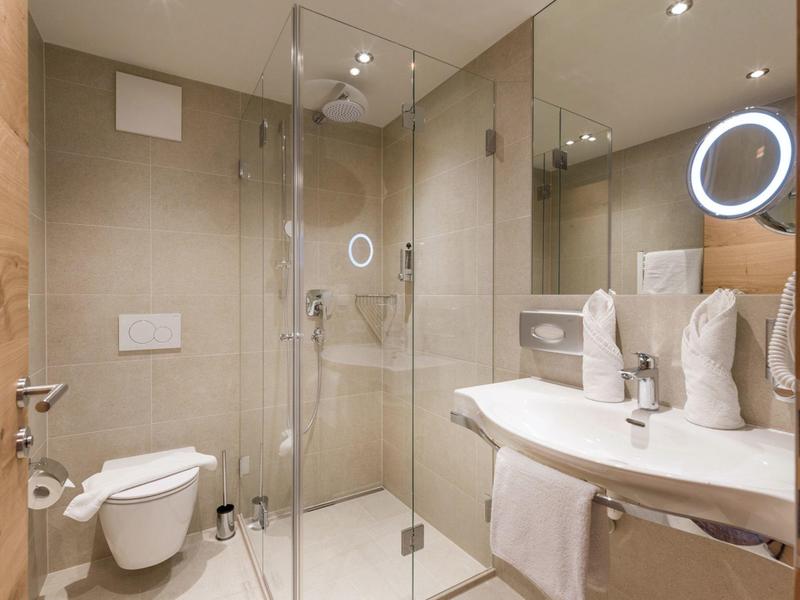 Modernes Badezimmer mit Glasdusche, Wand-WC, großem Spiegel und beleuchtetem Kosmetikspiegel.