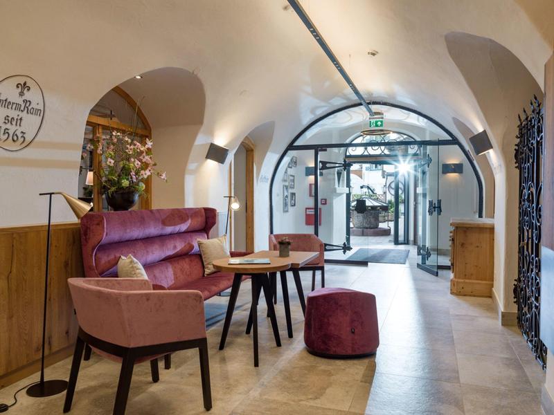 Moderner Sitzbereich mit rosa Polstermöbeln, Holztisch und gewölbter Decke in hellem Raum.