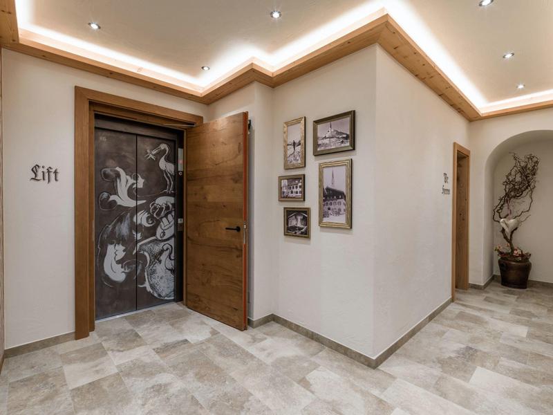 Moderner Flur mit Holzrahmen, Steinboden, beleuchtetem Deckenrand und dekorativem Aufzugstor.