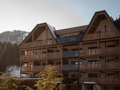 Mountain lodge with wooden balconies surrounded by trees and hills during sunset.