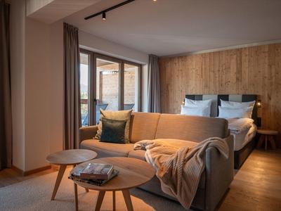 Cozy hotel room with sofa, two round tables, and a bed against wooden panel wall.