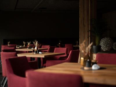 Cozy restaurant with red armchairs and wooden tables in dim lighting.