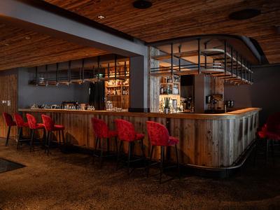 Cozy bar with wooden counter and red bar stools under warm wooden ceiling.
