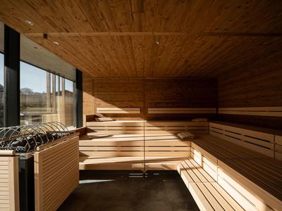 Interior of a wooden sauna with tiered benches and a heater by a window showing an outdoor view.